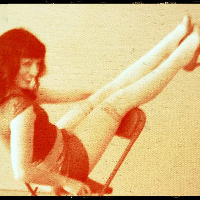 Roser Amills sentada en una silla plegable con las piernas levantadas, en una fotografía de tonos rojizos y aire retro