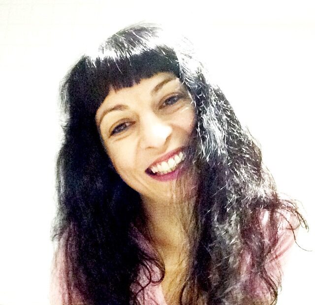Autorretrato de Roser Amills sonriendo, con el pelo suelto y flequillo, sobre fondo claro