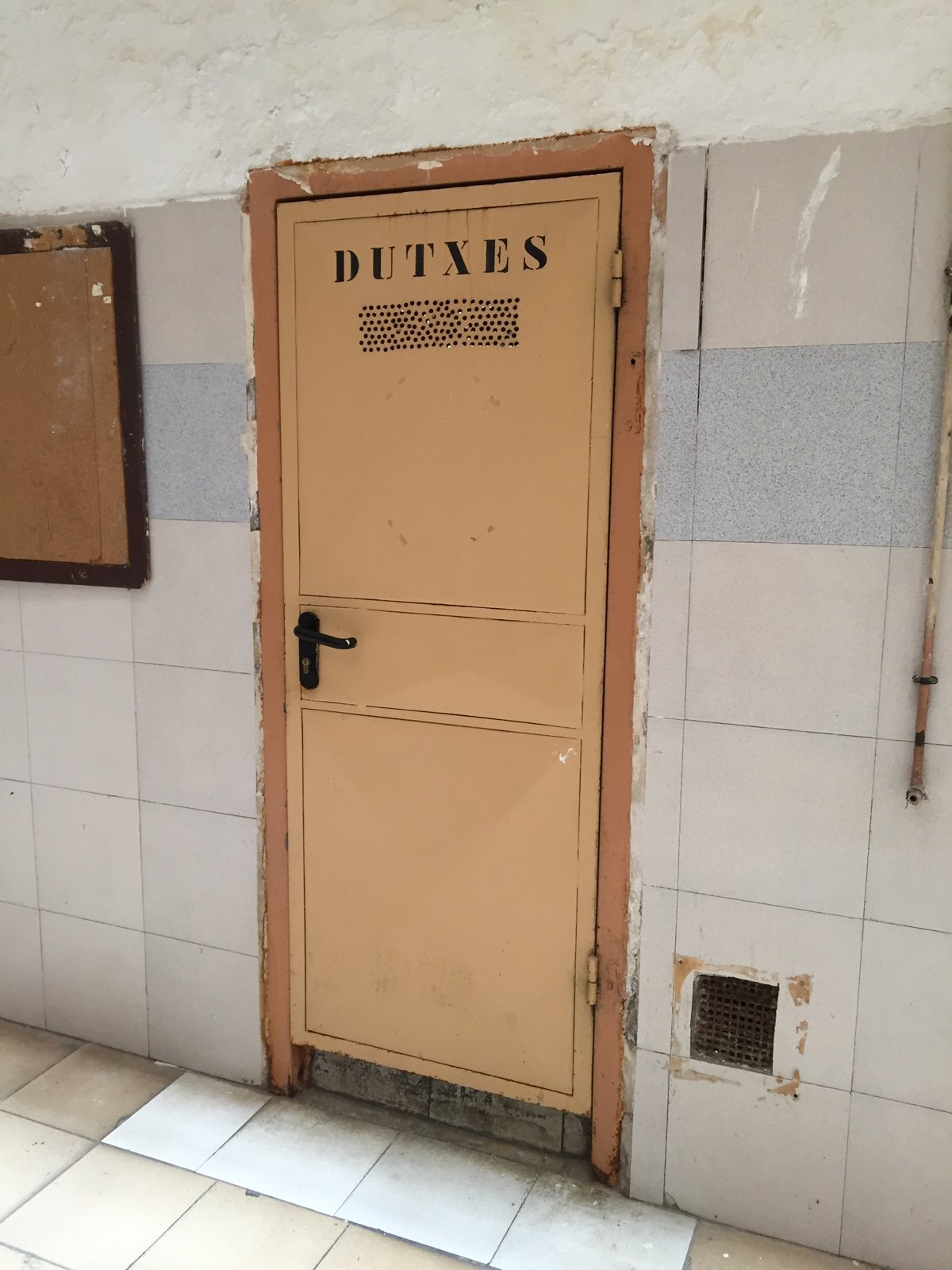 Puerta de color salmón con el rótulo «Dutxes» en una pared de azulejos blancos de La Model