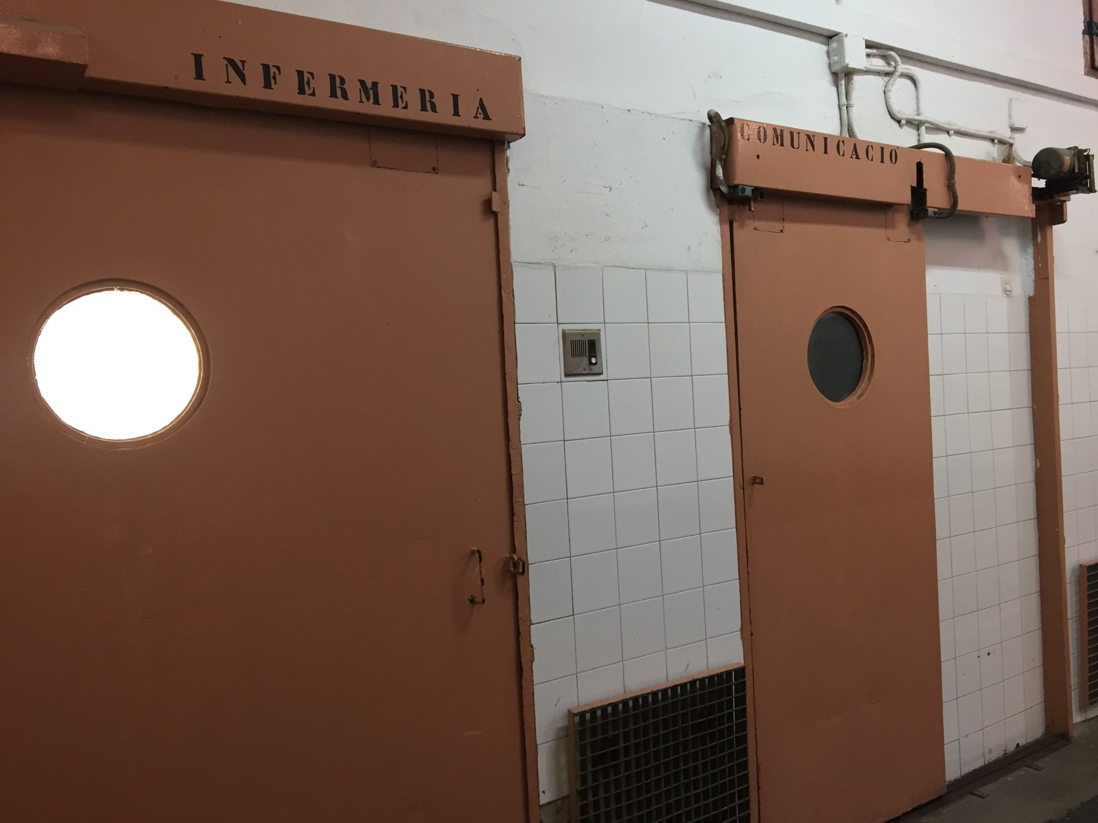 Puertas de color salmón con ventanucos redondos bajo el rótulo «Infermeria»