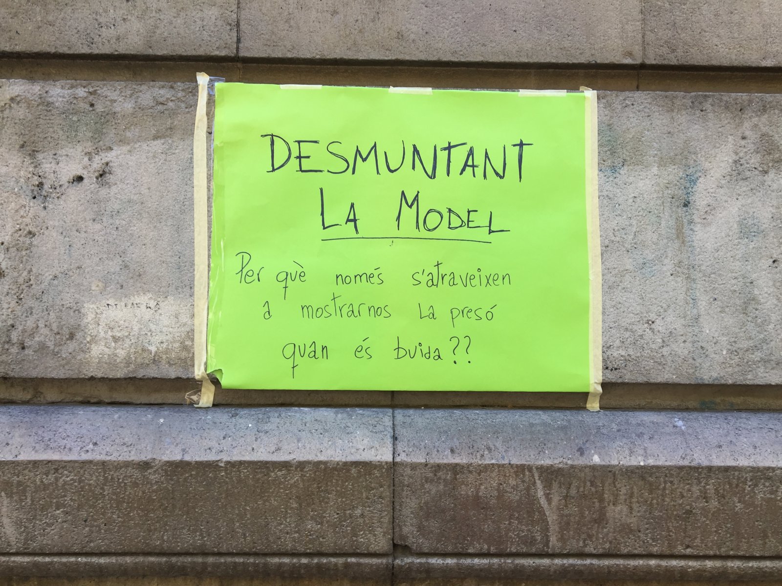 Cartulina verde pegada en un muro de La Model con el texto «Desmuntant la Model. Per què només s’atreveixen a mostrar-nos la presó quan és buida??»