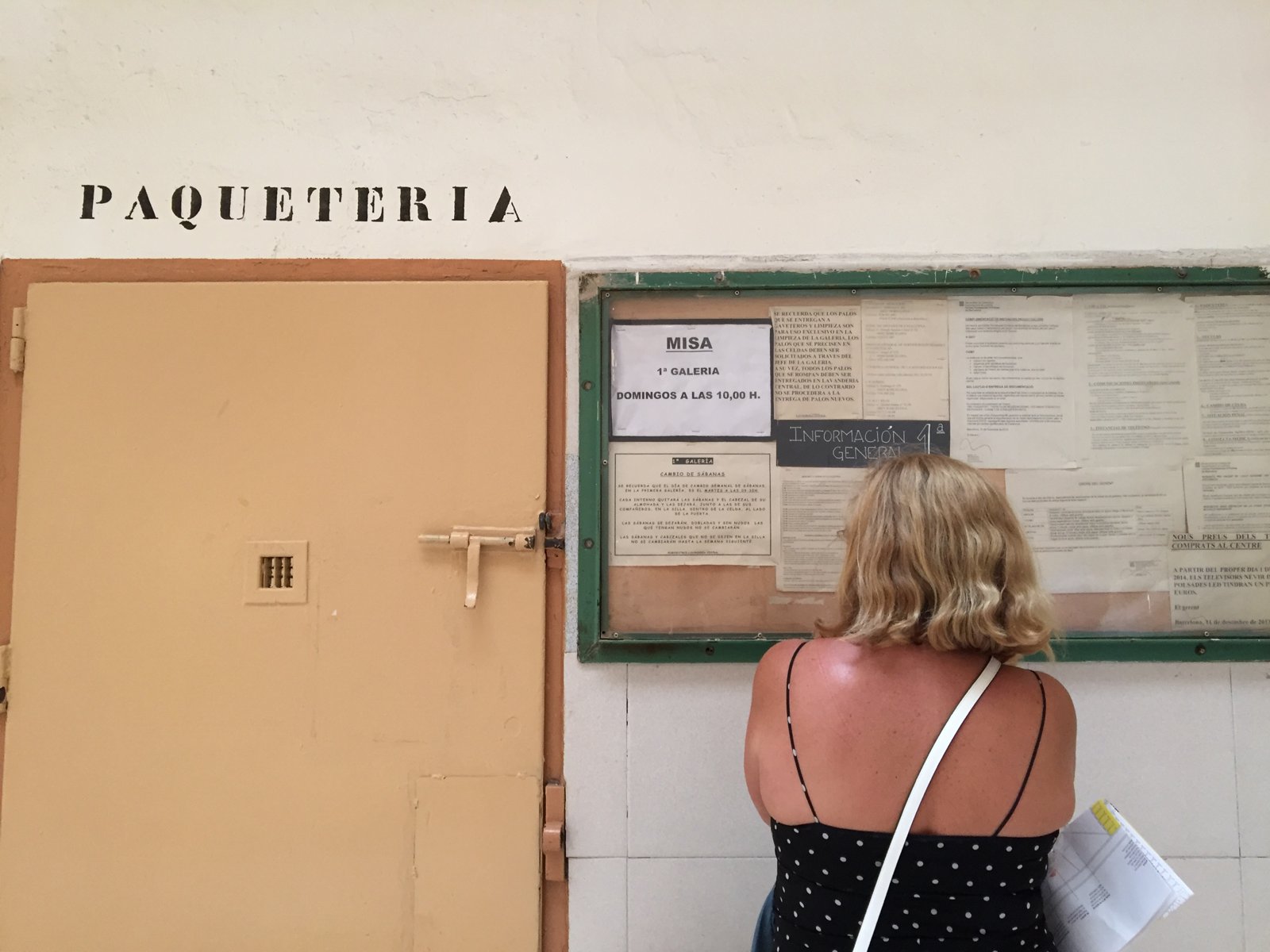 Puerta de color salmón con el rótulo «Paqueteria» junto a un tablón de anuncios que lee una visitante