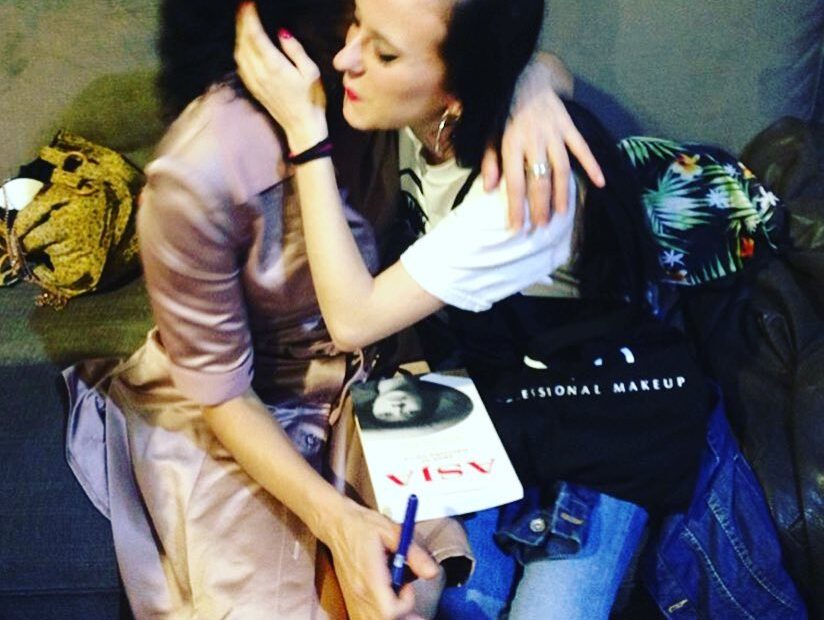 Roser Amills abraza a Laia Prat en un sofá, con un ejemplar de Asja sobre las rodillas