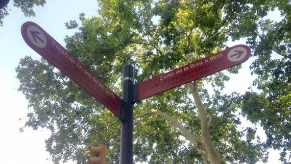 Señales de dirección rojas de una calle de Barcelona bajo las copas de los árboles, imagen de la columna Barcelona también es tipografía