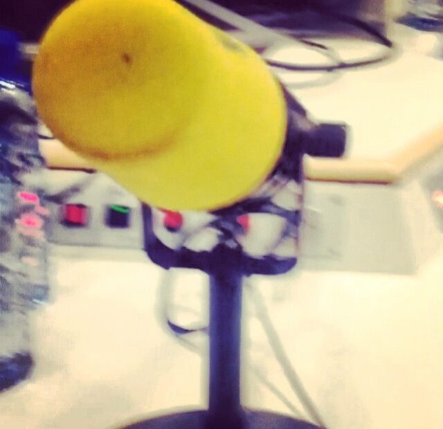 Micròfon groc de l’estudi de Catalunya Ràdio, vist de prop, amb la taula de control al fons