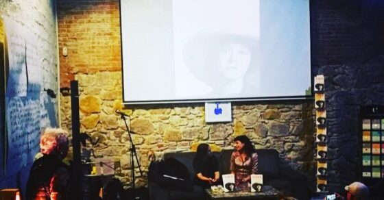 Roser Amills y M. Àngels Jover conversan sentadas ante el público, con la cubierta de Asja proyectada en la pantalla