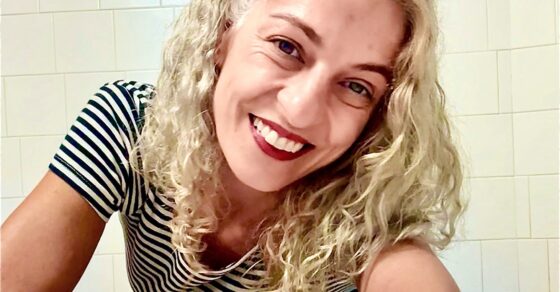 Roser Amills sonríe apoyada en una mesa, con camiseta de rayas blancas y negras.