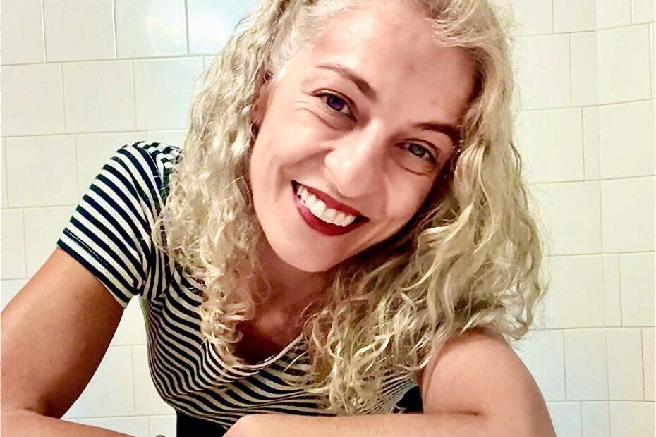 Roser Amills sonríe apoyada en una mesa, con camiseta de rayas blancas y negras.