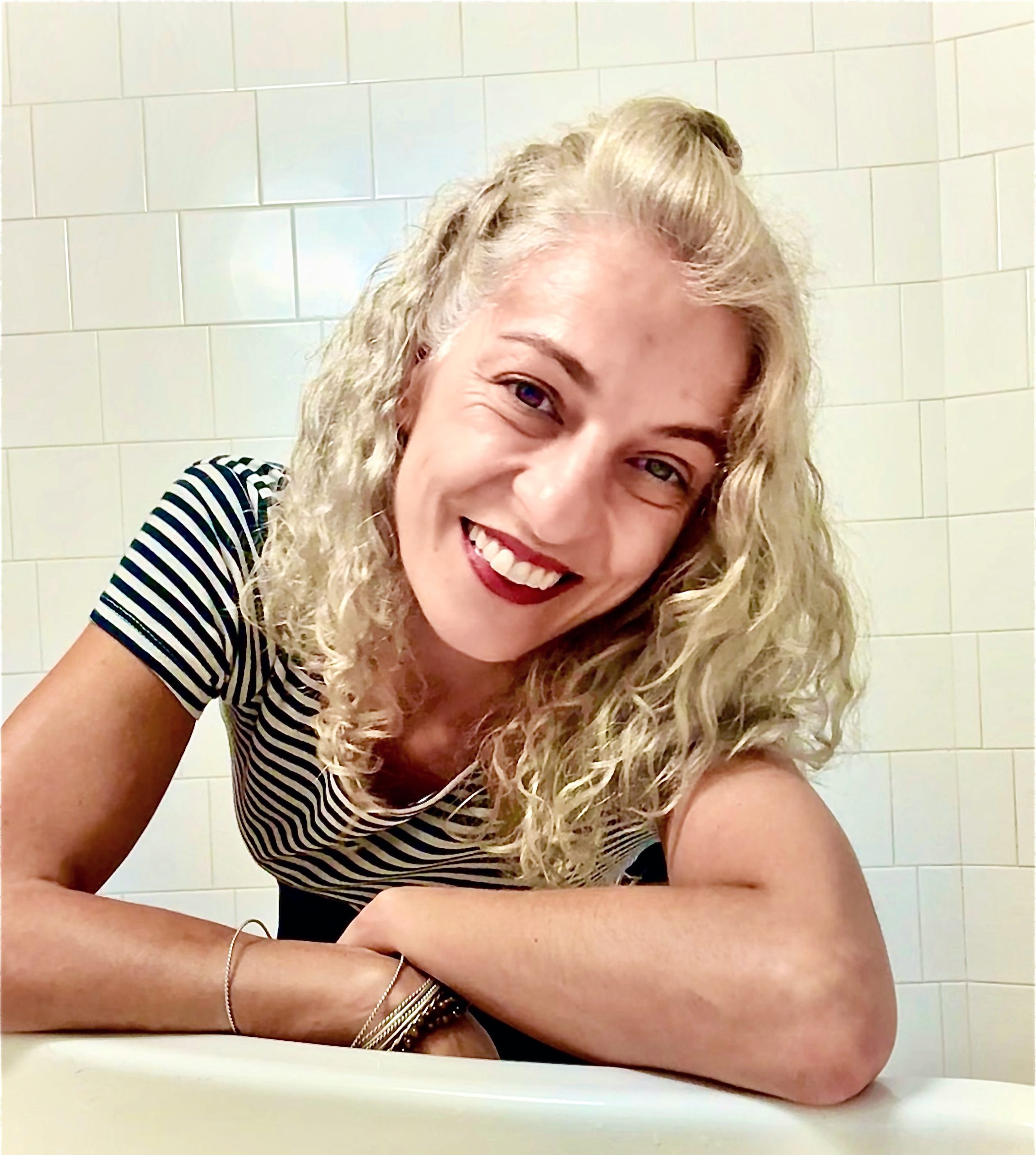 Roser Amills sonríe apoyada en una mesa, con camiseta de rayas blancas y negras