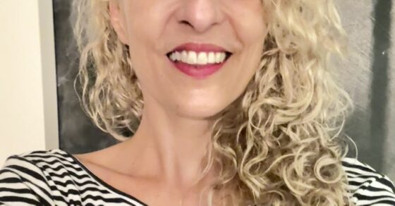 Primer plano de Roser Amills sonriendo, con camiseta de rayas, ante un fondo oscuro.
