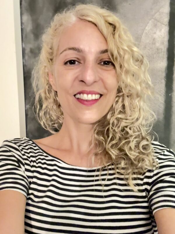 Primer plano de Roser Amills sonriendo, con camiseta de rayas, ante un fondo oscuro.
