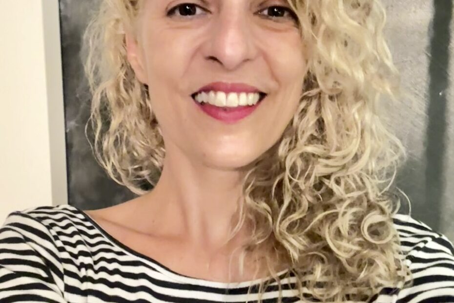 Primer plano de Roser Amills sonriendo, con camiseta de rayas, ante un fondo oscuro.