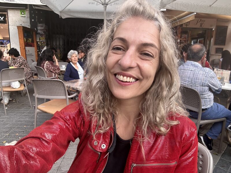 Roser Amills, con chaqueta roja, sonríe en una terraza.