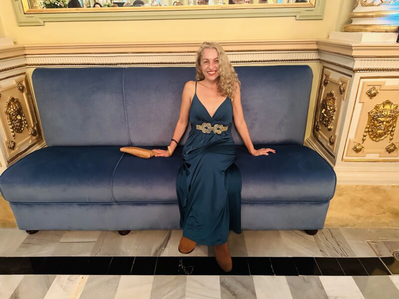 Roser Amills, con vestido largo, sentada en un sofá de terciopelo azul.