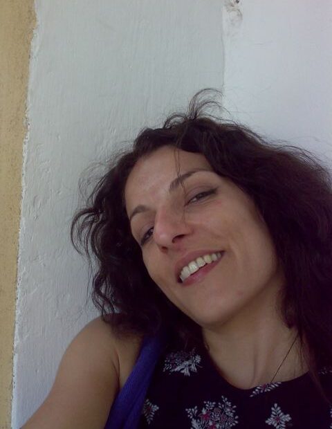 Autorretrato de Roser Amills sonriendo con la cabeza ladeada junto a una pared blanca