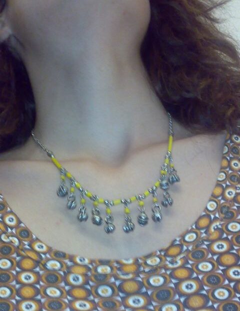 Cuello y escote de Roser Amills con un collar de cuentas amarillas y cascabeles plateados, sobre un vestido estampado