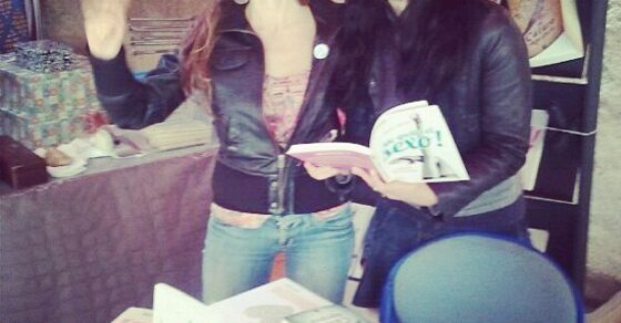 Roser Amills, con un ejemplar abierto, junto a una lectora que saluda en la mesa de firmas de M’agrada el sexe! en Arnes, el 26 de mayo de 2013