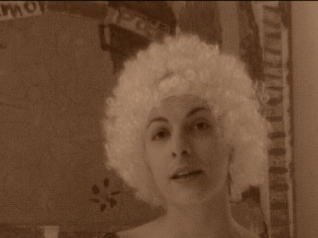 Roser Amills, con peluca blanca rizada, mira a la cámara en una foto en tono sepia