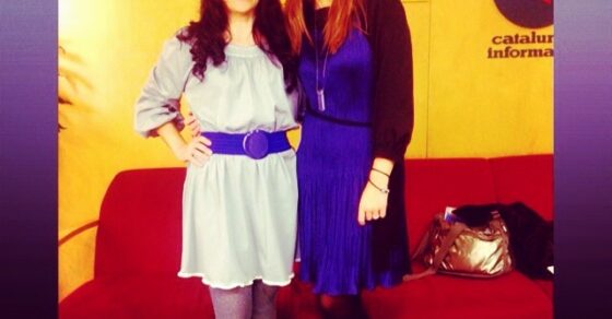 Roser Amills, con vestido gris y cinturón morado, junto a Carme Sánchez, con vestido azul, ante un sofá rojo