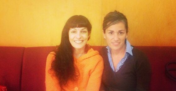 Roser Amills, con rebeca naranja, y Emma Ribas, sentadas en un sofá rojo bajo el rótulo de Catalunya Informació