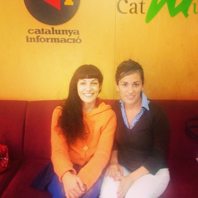 Roser Amills, amb rebeca taronja, i Emma Ribas, assegudes en un sofà vermell sota el rètol de Catalunya Informació