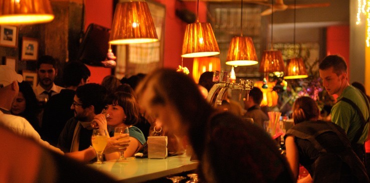 Gent prenent copes en un bar ple, amb làmpades penjants